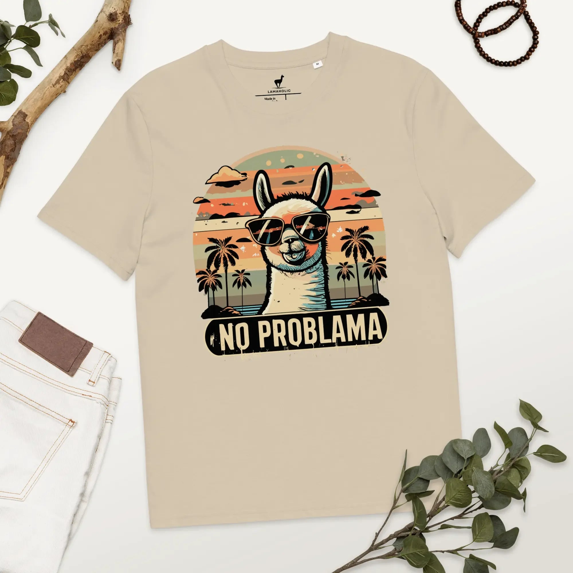 Lustiges Lama T-Shirt in Desert Dust mit "No Problama" Design, flach liegend auf einem Holztisch.